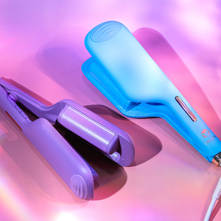 Two colorful Calista Tools BodyWaver Large Wave Stylers in purple and blue are displayed on a shiny pink and purple background with soft light reflections.