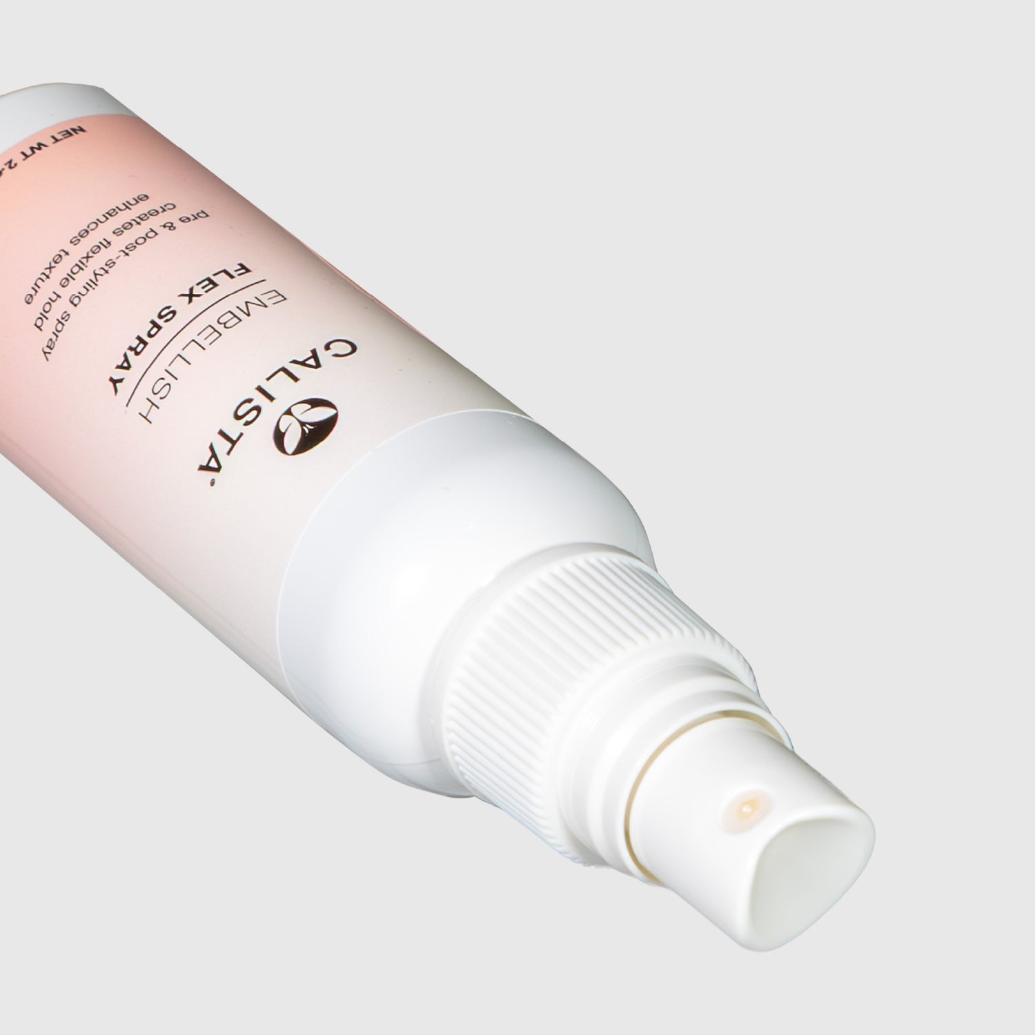 A close-up of a white spray bottle labeled Calista Tools Mini EMBELLISH Flex Spray, a non-aerosol hairspray, lies on its side with the nozzle facing forward against a light gray background.
