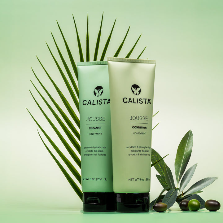 Two green JOUSSE Cleanse bottles by Calista Tools with leafy accents stand upright on a green background, highlighting keratin amino acids for healthy hair growth. A palm frond and olives complete the natural, fresh vibe.