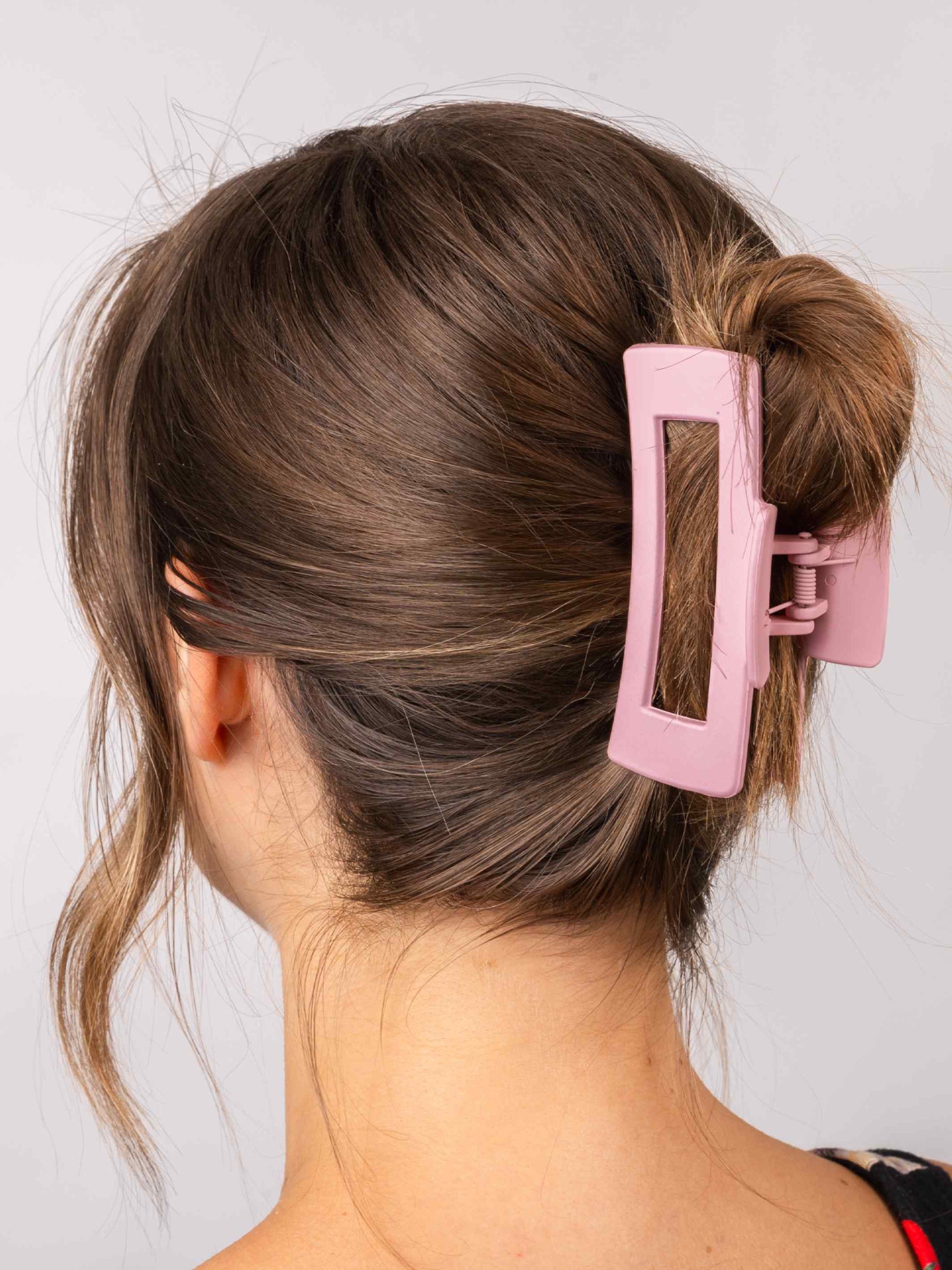 A woman with brown hair in a loose bun, secured from behind with the Calista Claw Clip by Calista Tools in pink for strong hold. A few strands hang loose on the sides.