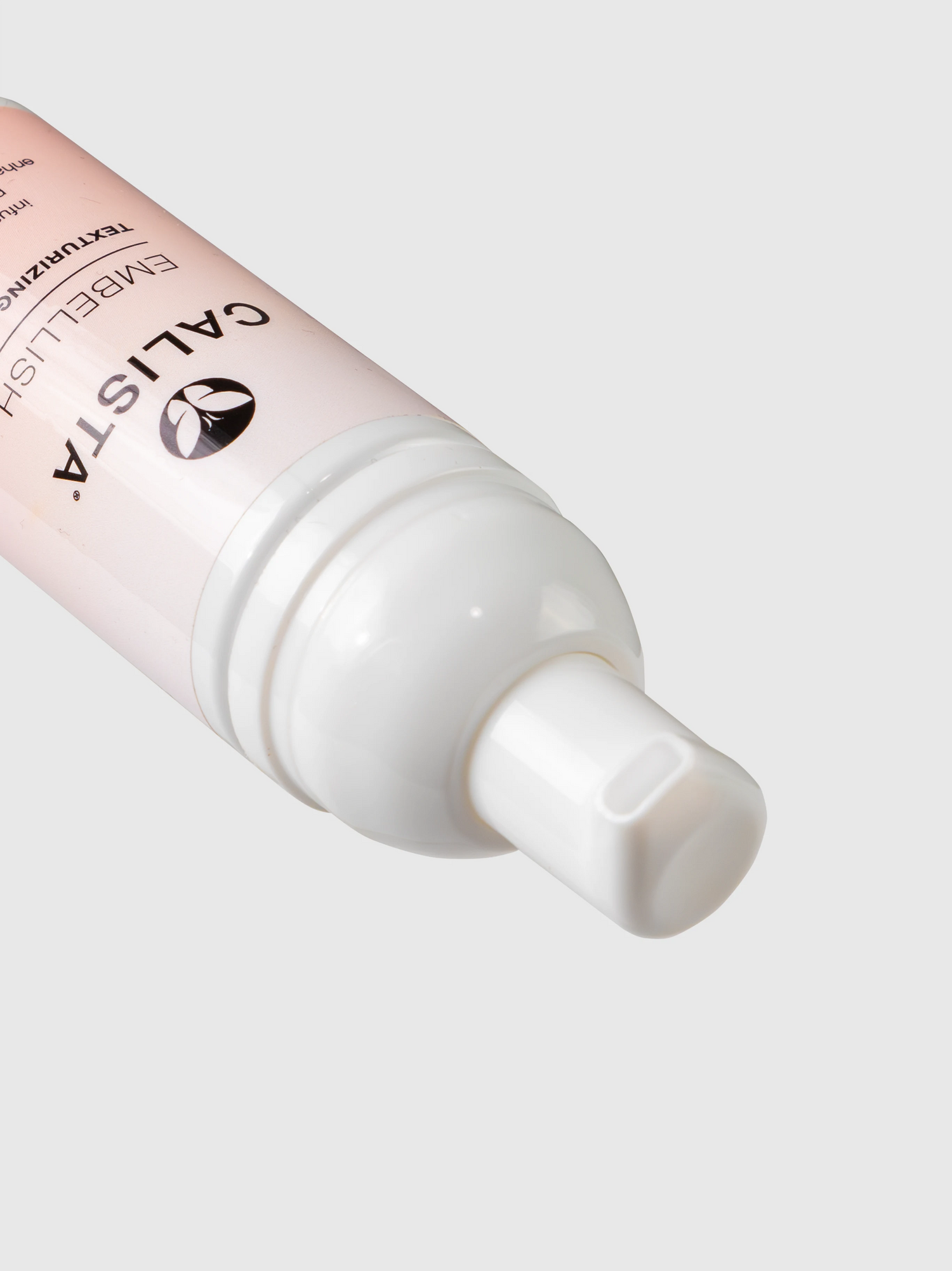 A close-up of a white pump dispenser bottle labeled Calista Tools, featuring Mini EMBELLISH Texturizing Foam, set diagonally on a light pink surface with a simple light gray background.