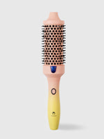 The Calista Tools Vault FAUXblo Thermal Blowout Brush 1.77" is a cylindrical, pink and yellow heated round brush with black bristles and power button, designed to dry and volumize hair.