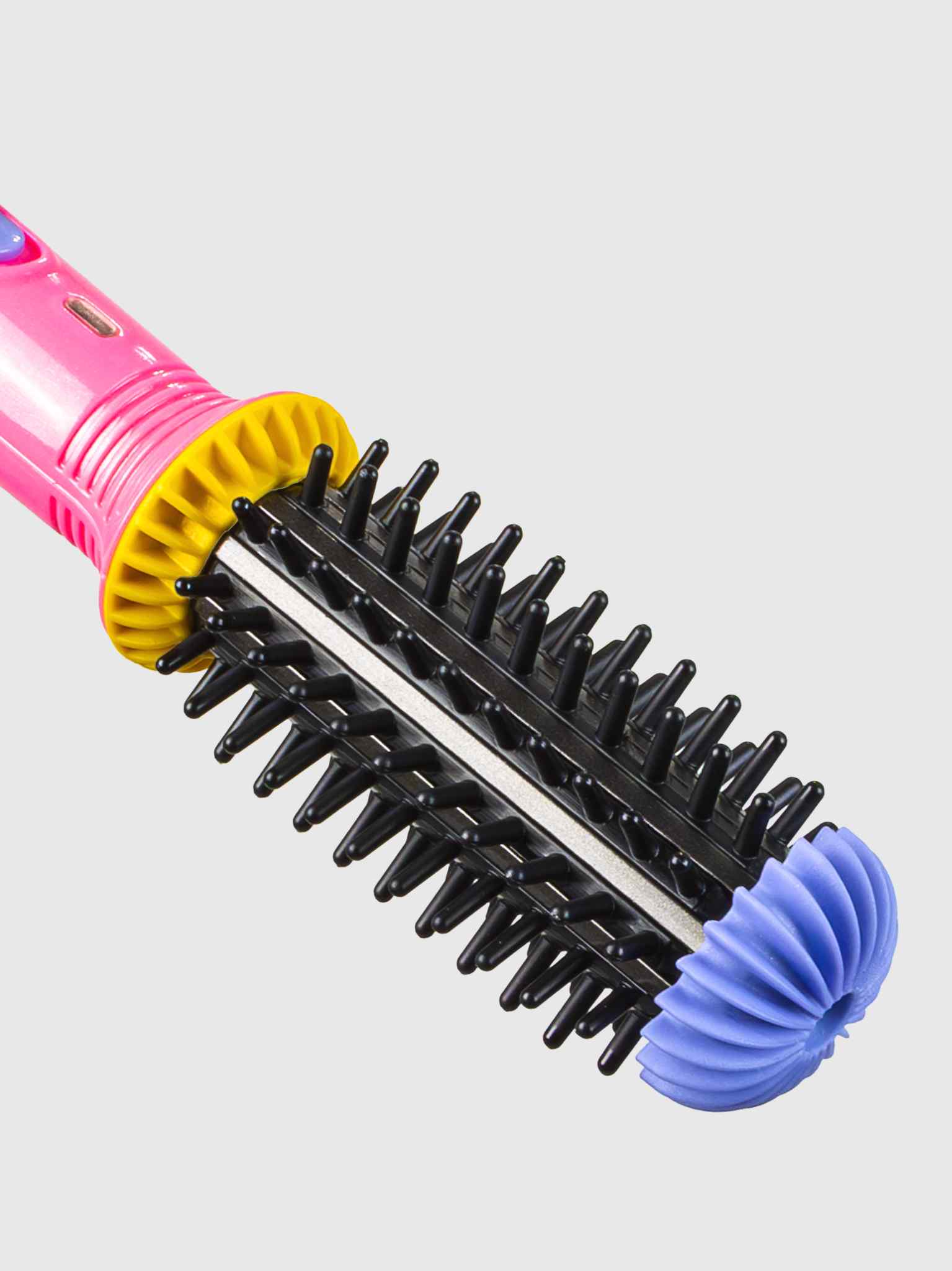 A close-up of the Calista Tools GoGo Mini Round Brush & Embellish Flex Spray Duo shows its pink brush with black bristles, yellow and blue end caps, against a light grey background—ideal as a travel hair brush.