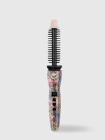 The Refurbished Perfecter Pro Heated Round Brush by Calista Tools features a floral pattern, black bristles, digital display, and control buttons—an elegant styling tool that stands upright against a plain light background.