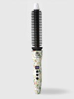 The Refurbished Perfecter Pro Heated Round Brush by Calista Tools, featuring a floral pattern, cylindrical barrel, black bristles, digital display, and white tip, stands upright against a light gray background—a chic styling tool.