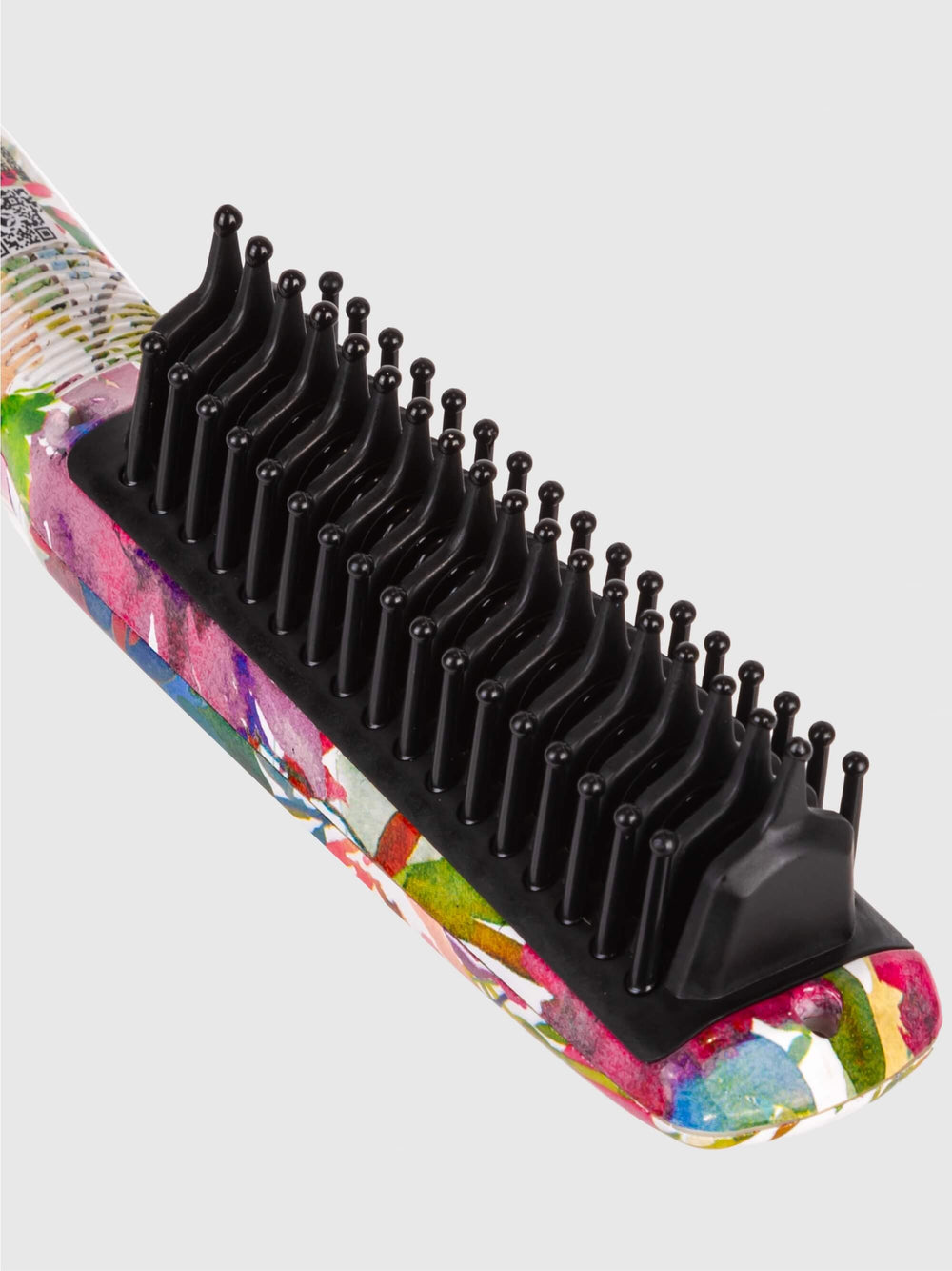 Close-up of the Calista Tools Triangl Pro Heated Detailer Brush, featuring black bristles, a floral-patterned handle, and unique triangular plates for effective de-frizz hair styling, set against a plain light background.